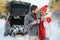 Couple in love sitting in car trunk drinking hot tea in snowy winter forest and chatting. People relaxing outdoors during road