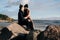 Couple in love sitting on the stone near the ocean, hugging and enjoy each other.