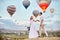 Couple in love stands on background of balloons in Cappadocia. Man and a woman on hill look at a large number of flying balloons