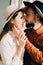 A couple in love in trendy clothes and hats are sitting on a brown sofa, embracing in a spacious beautiful Studio. family concept