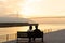 Couple in love watching sunset together on ocean travel summer holidays. People silhouette from behind sitting enjoying view.