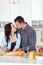 Couple making fresh organic juice in kitchen together. A young woman in a blue shirt slices a baguette. A man is hugging