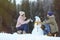 Couple making snowman near forest.