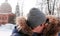 Couple man and woman kisses and walking in winter city park in snowy day with falling snow.