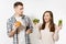 Couple man and woman standing with green detox smoothies, salad in glass bowl, burger, cola in glass bottle isolated on