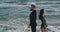 Couple of man and woman in swimming suits. Spectacular couple standing against sea waves in black suits. Brunette with