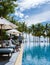 Couple of men and women relaxing by the pool in beach beds chairs, tropical pool