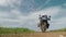 A couple of motorcyclists ride a touristic motorcycle on a dirt road. Green fields beyond the horizon. Summer day. The concept of