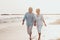 Couple of old mature people walking on the sand together and having fun on the sand of the beach enjoying and living the moment.