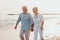 Couple of old mature people walking on the sand together and having fun on the sand of the beach enjoying and living the moment.