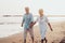 Couple of old mature people walking on the sand together and having fun on the sand of the beach enjoying and living the moment.