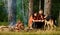 Couple play with german shepherd dog near bonfire, forest background.