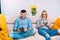 Couple playing digital video games with joystick controller while sitting on sofa or couch.
