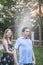 Couple playing with a garden hose and spraying each other outside in the garden, man has a shocked look