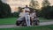 Couple posing golf cart outside. Two golfers take clubs sport equipment on field