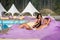 Couple relaxing near swimming pool on cushioned loungers with drinks at the luxury resort