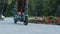 Couple rides on rented electric scooters past flower bed in park, low angle, front view . Man and woman ride on electric