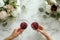 Couple on romantic date. Friends clinking glasses, top view. Red wine, flowers around on marble table. Wedding celebration, party