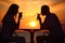 Couple\'s silhouettes on sunset drink from glasses