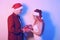 Couple in santa hats, new year, christmas. Lovers in neon light. Guy gives a gift in a red box to a happy girl, surprised woman in