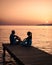 couple seated on a wooden jetty, looking a colorful sunset on the sea , men and woman watching sunset in Crete Greece