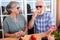 Couple of senior people, gray and white hair sitting outdoor at a wooden table. Eating a sandwich and some fruits with a redwine