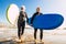 Couple of seniors at the beach with black wetsuits holding a surftable ready to go surfing a the beach - active mature and retired