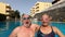 Couple of seniors enjoying summer and having fun together in the pool swimming and smiling looking at the camera - cheerful happy