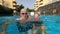 Couple of seniors enjoying summer and having fun together in the pool swimming and smiling looking at the camera - cheerful happy