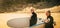 Couple of seniors going surfing together - two mature people in the beach with surfboards and wetsuits looking at the sea on the