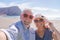 Couple of seniors travelling and taking a selfie in a beautiful beach with a mountain at the background - smiling and ejoying