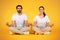 Couple in serene meditation, sitting in lotus position, yellow background