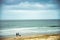 Couple silhouetted with dog walk along the seashore, with moody, cloud sky background.