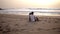 A couple sit in the sand at the beach looking out to the ocean and kiss in the sunset. Sensual scene of two loving