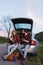 Couple sit on the trunk of car and wonder at photo on tablet