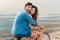 couple sitting on bicycle on beach near sea and looking