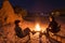 Couple sitting at burning camp fire in the night. Camping in the desert with wild elephants in background. Summer adventures and e