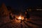 Couple sitting at burning camp fire in the night. Camping in the desert with wild elephants in background. Summer adventures and e