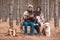 A couple are sitting in an forest with a labrador, drinking tea covered in blanket and laughing. Outdoors.