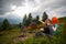 Couple sitting on the green grass near campfire, tents, backpacks