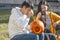 Couple sitting outside on campus carving pumpkin jack-o-lantern with girl videoing him working