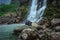 Couple sitting at rock in front of waterfall water stream falling from mountains long exposure