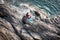 Couple sitting on rugs on rocks looking out to sea.