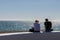 A couple sitting on a wall at the seaside on a summers day enjoying the view of the sea