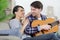 couple snuggled on sofa while man plays guitar