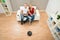 Couple On Sofa With Robotic Vacuum Cleaner On Floor