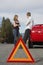 Couple Standing By Breakdown Car With Warning Triangle In Foreground