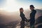 Couple stands, holds hands and looks at each other against background of sunrise in mountains.