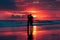 A couple stands on a sandy beach, gazing out at the picturesque coastal sunset. The pair is embracing, captivated by the