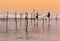 A couple of Stilt fishermen sitting on their poles with wooden fishing rods in their hands in the sunset evening. Ocean waves